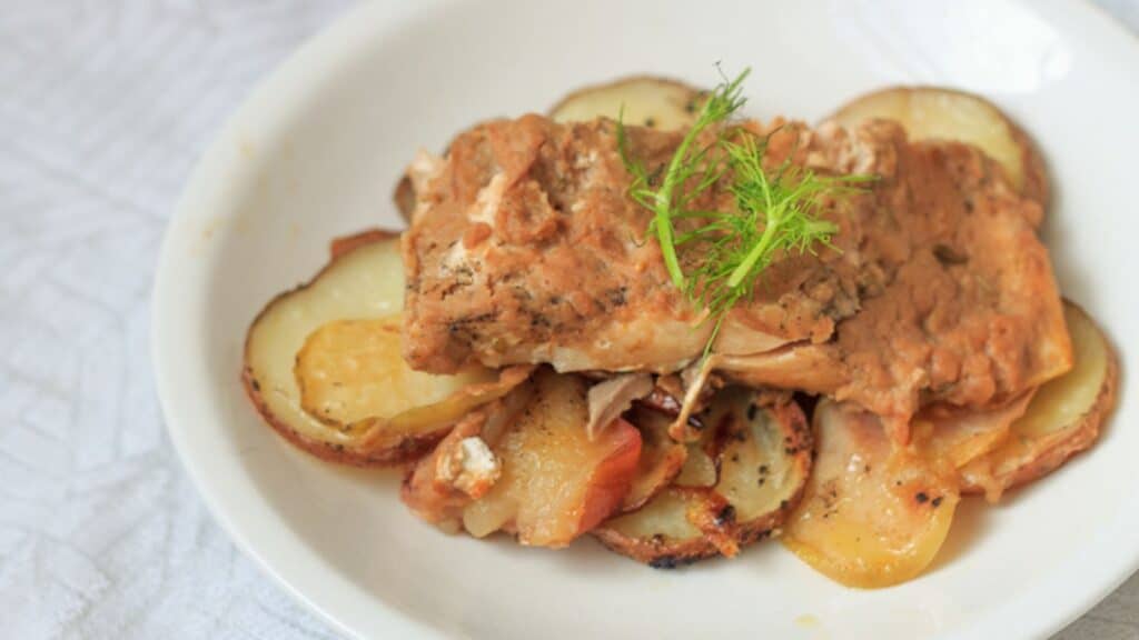 A white plate with a piece of fish and potatoes.