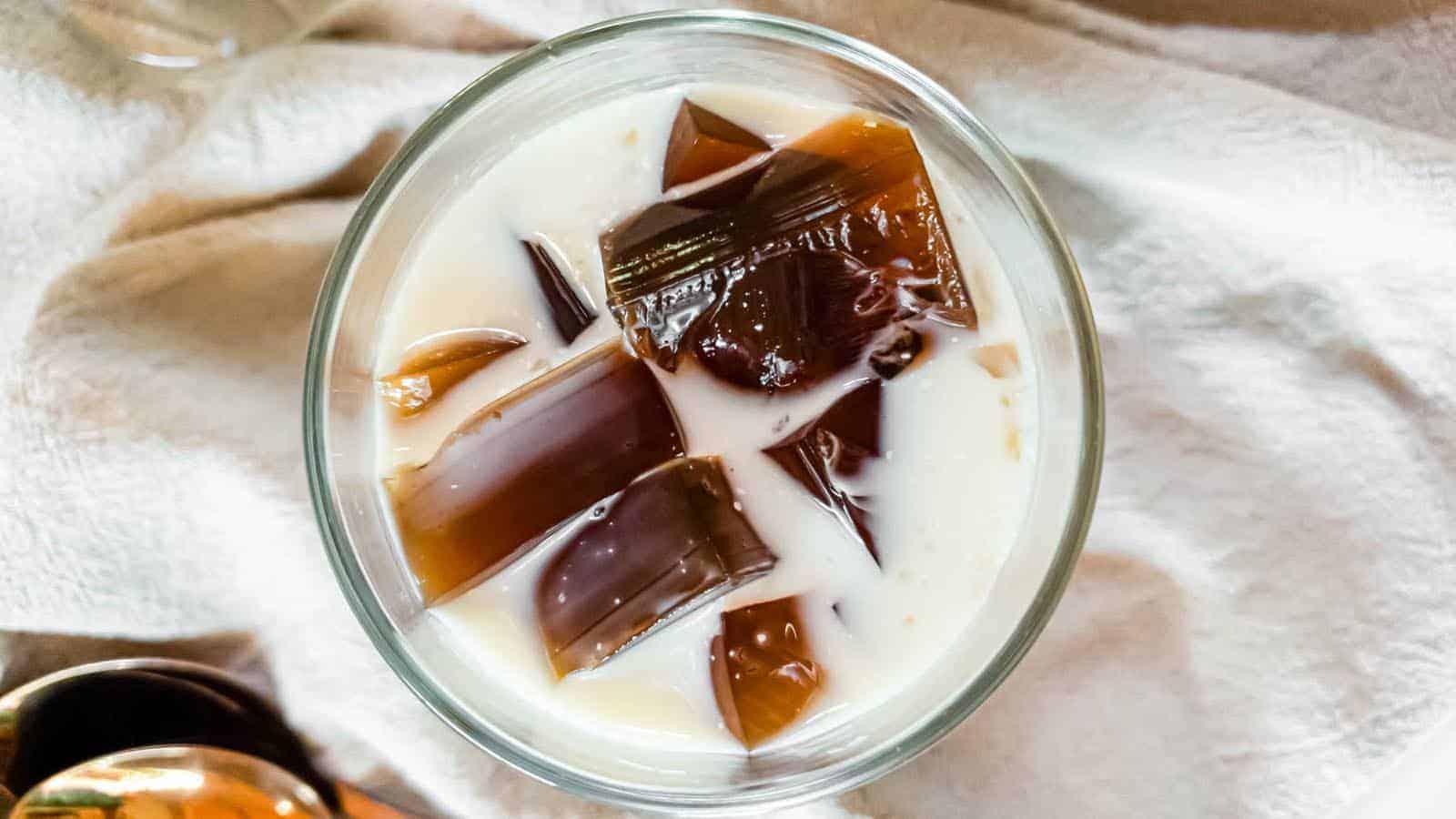 A glass of coffee jelly with heavy cream on a fabric background.