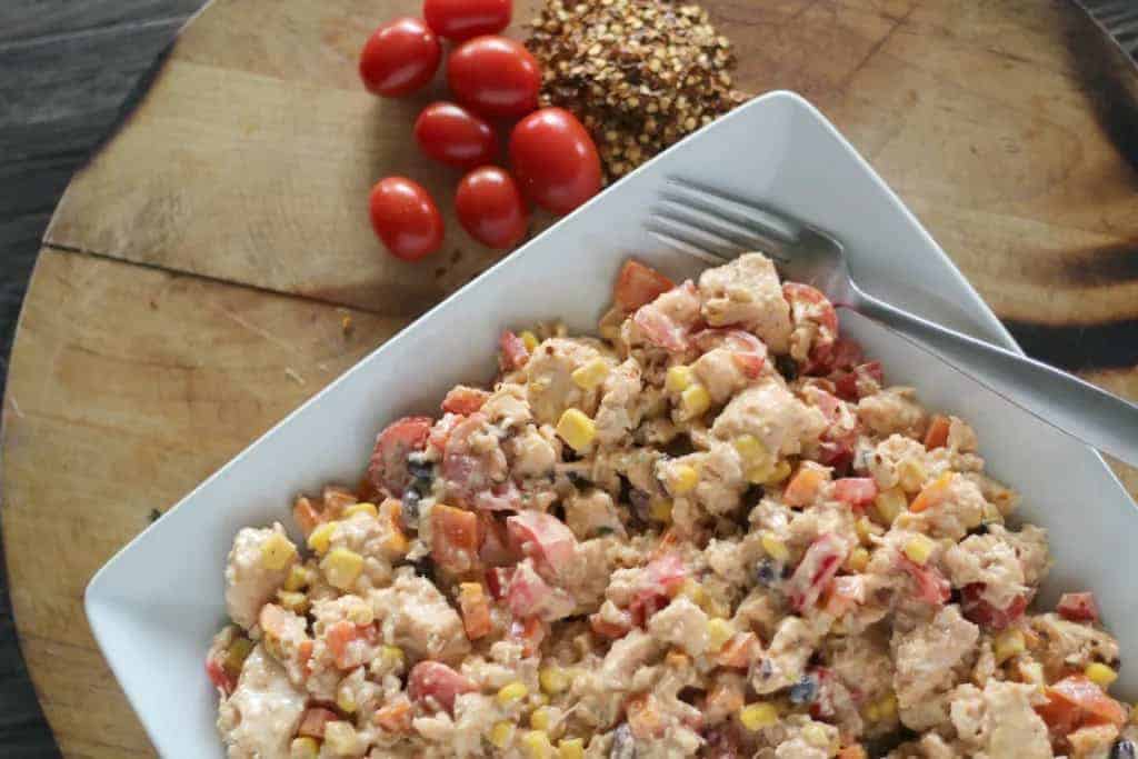 Plate of chicken salad next to spices and tomatoes.