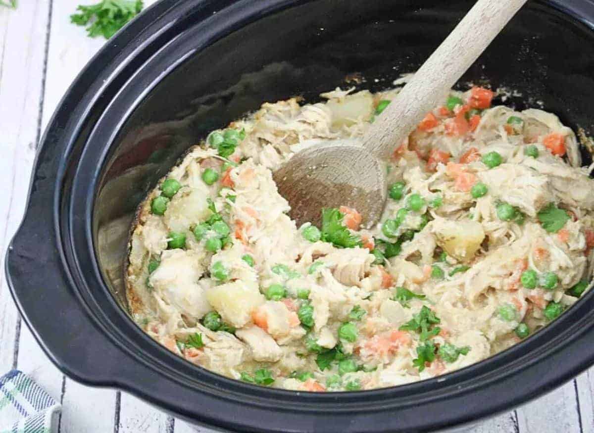 Wooden spoon scooping our dairy-free chicken pot pie from a slow cooker.