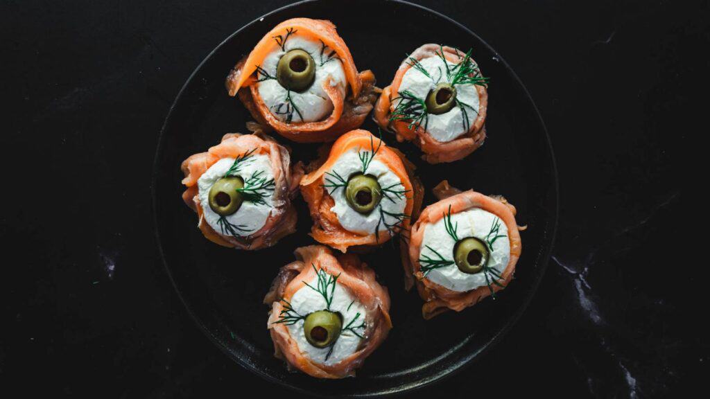 Smoked salmon with olive eyes on a black plate.