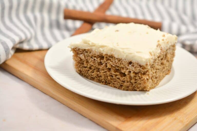 A piece of cake on a plate with cinnamon sticks.