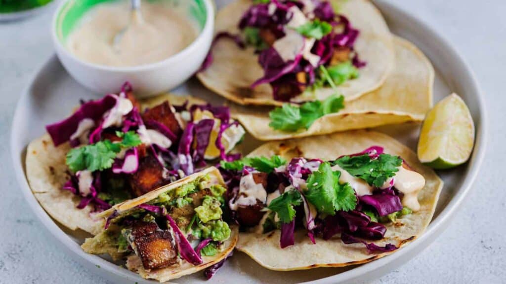 A plate of fish tacos with slaw and dipping sauce.