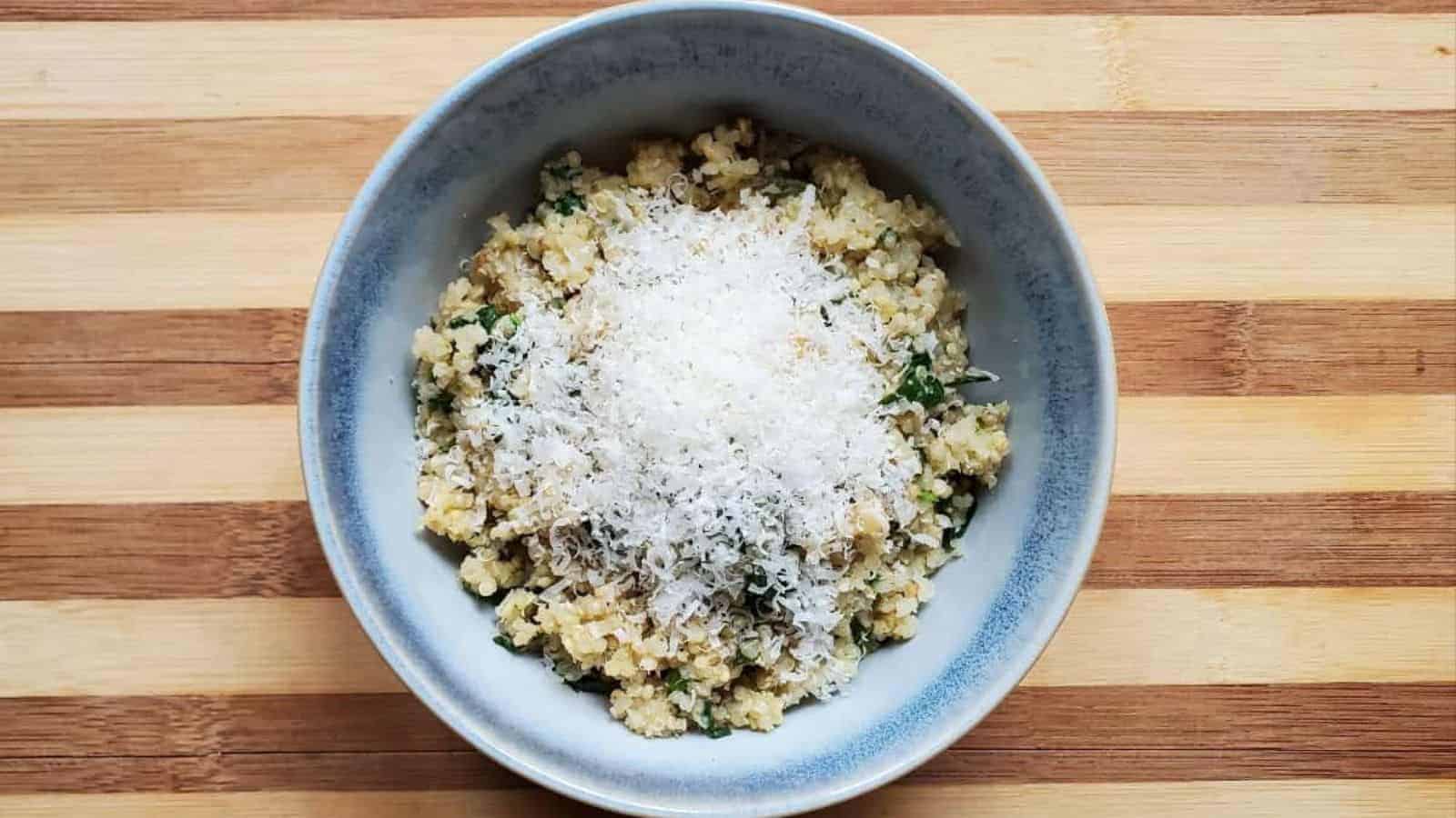 Image shows an overhead shot of Spinach Parmesan Quinoa in a blue bowl with a sprinkle of cheese on top.