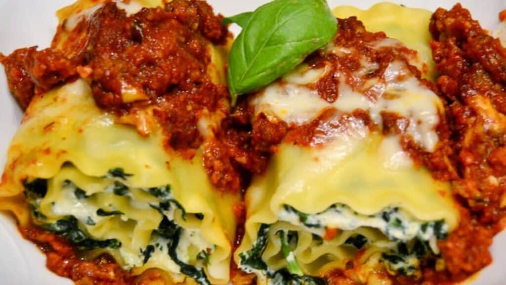 A plate of cheesy lasagna rolls with sauce and basil.