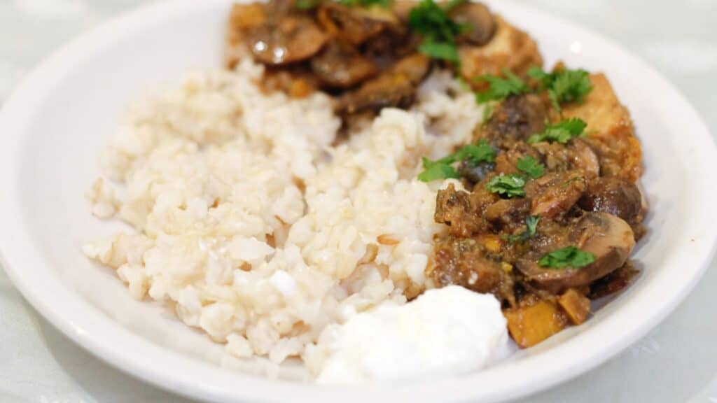 A white bowl with rice, mushrooms and sour cream.