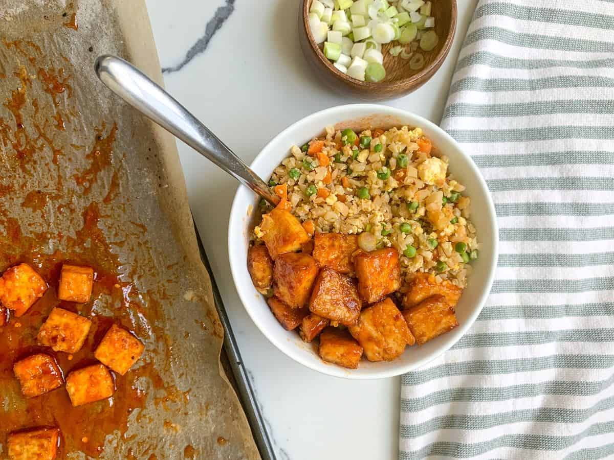 A bowl of cauliflower rice and tofu on a table.