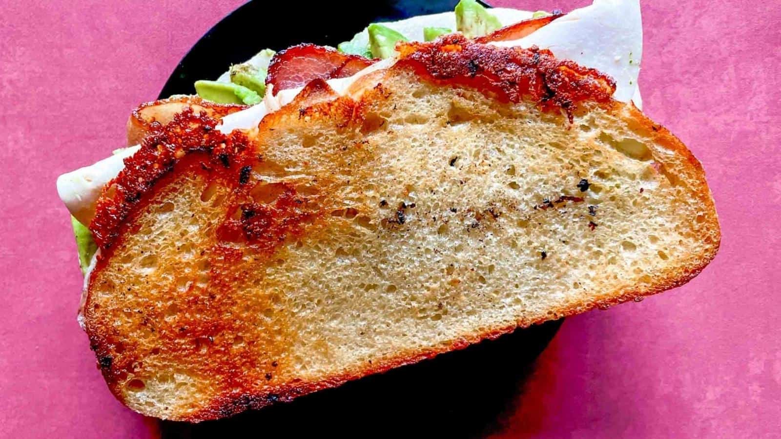 A turkey avocado sandwich sits on a red background.