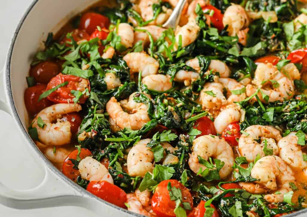 A pan full of shrimp, tomatoes and spinach.