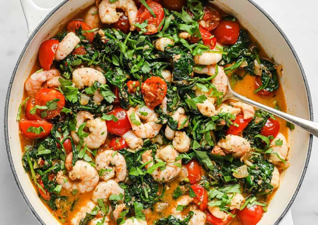 A pan with shrimp, tomatoes and spinach in it.