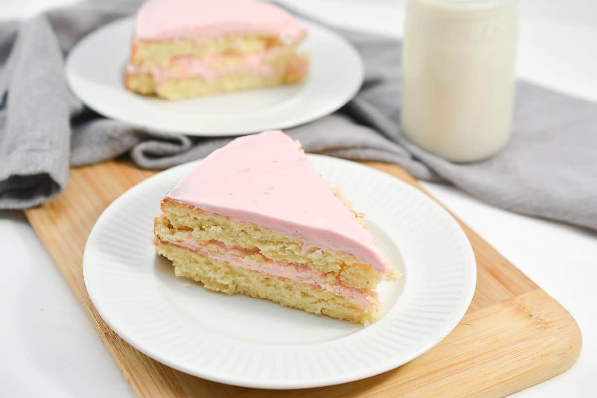 A slice of pink cake on a plate next to a glass of milk.