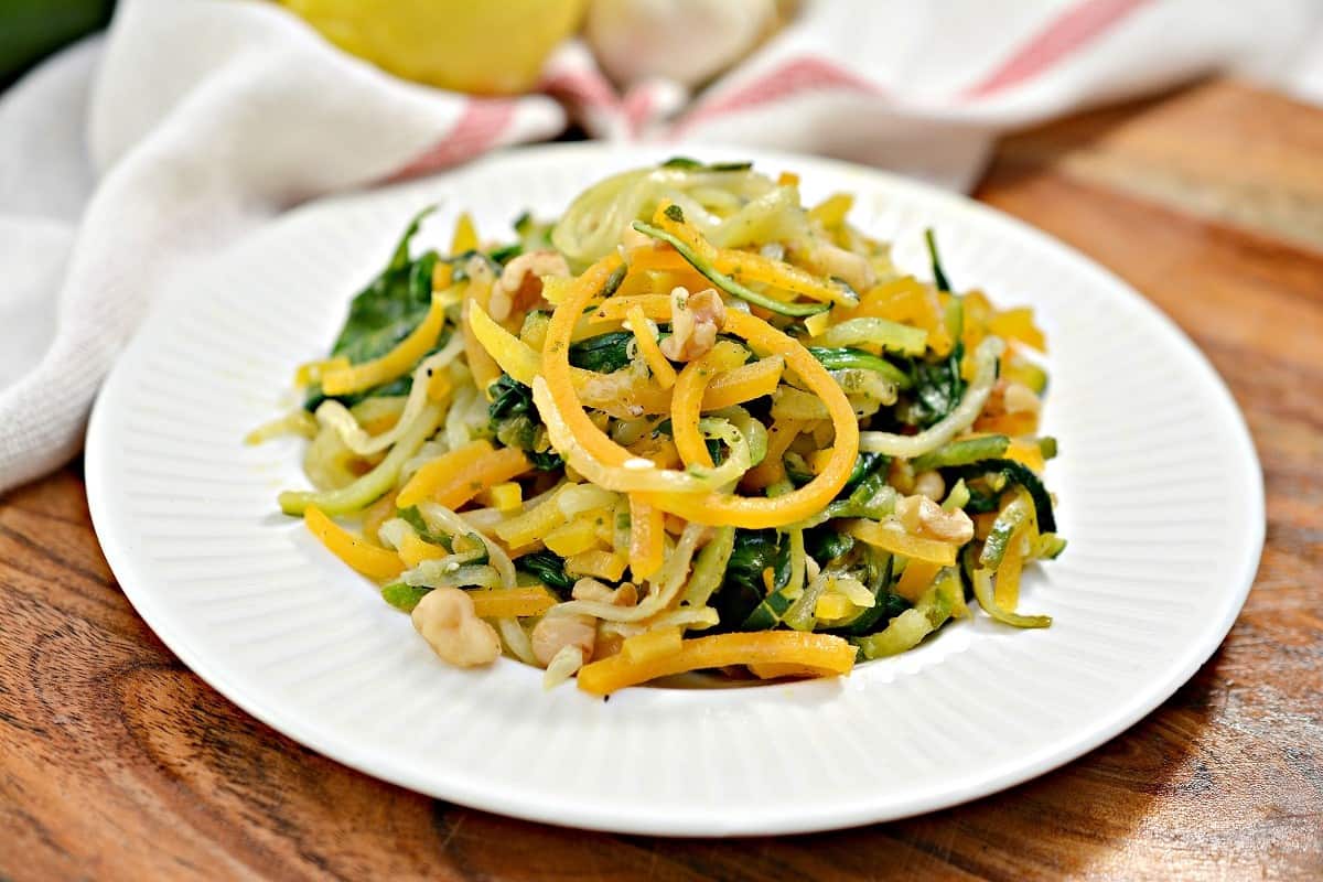 Zucchini noodles with cashews and lemons on a white plate.