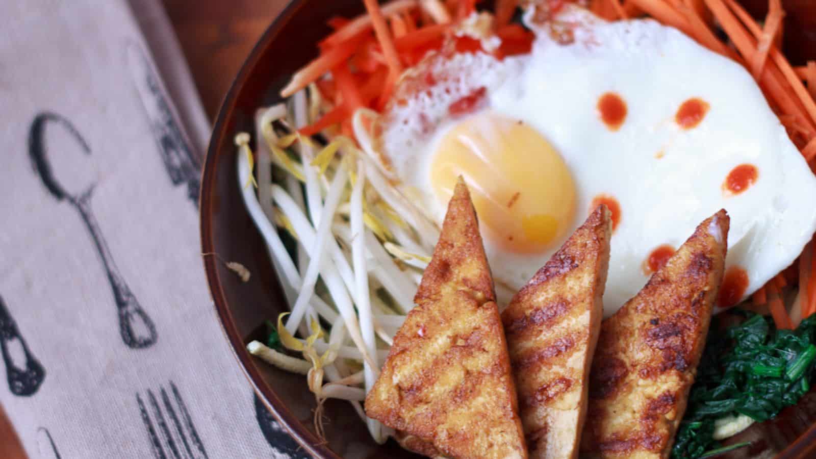 A bowl of tofu and vegetables with an egg on top.