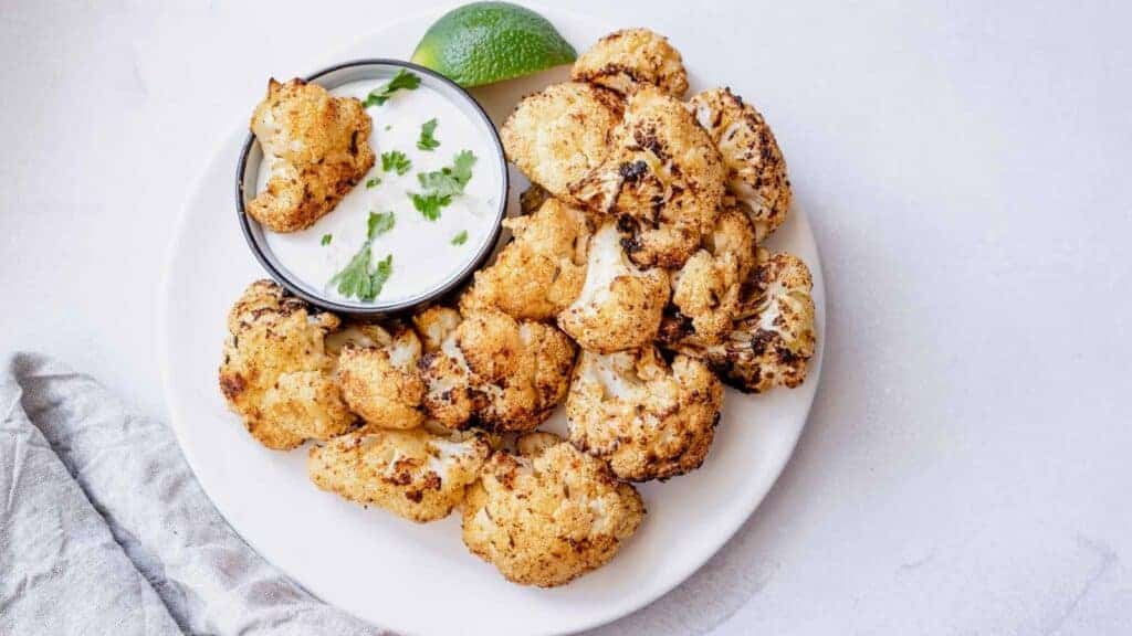 Cauliflower florets with dipping sauce on a white plate.