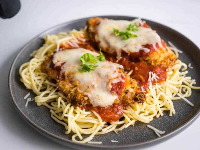 Chicken parmigiana on a plate with spaghetti and sauce.