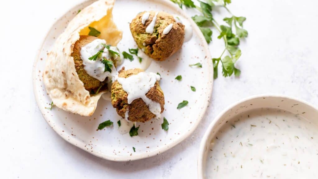 Gyro meatballs with tzatziki sauce on a white plate.