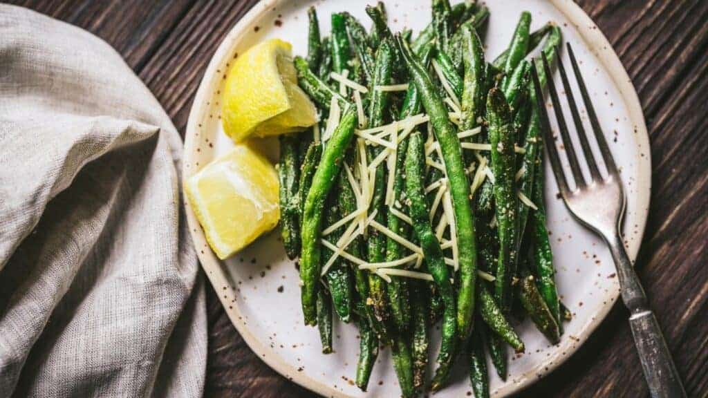 Roasted green beans on a plate with lemon wedges.