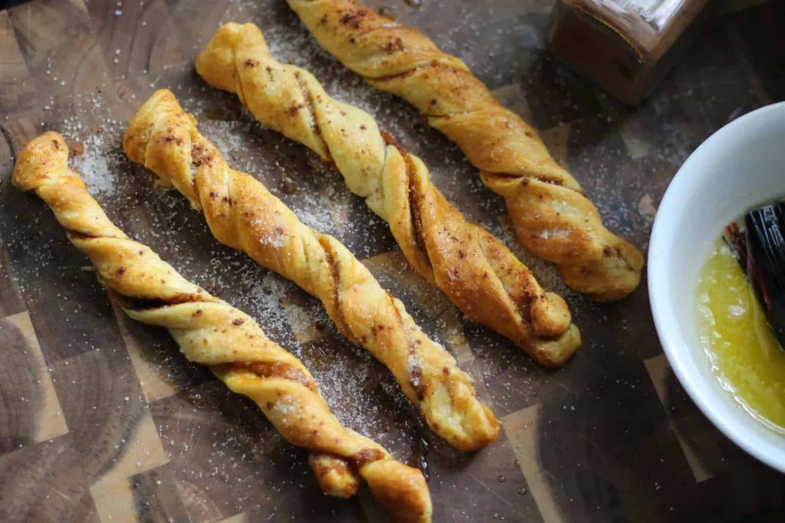 Pumpkin spice churros on a wooden serving board with a bowl of butter off to the right side.