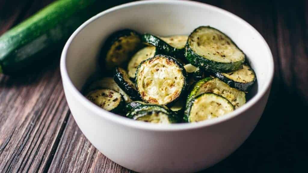 Grilled zucchini in a white bowl on a wooden table.