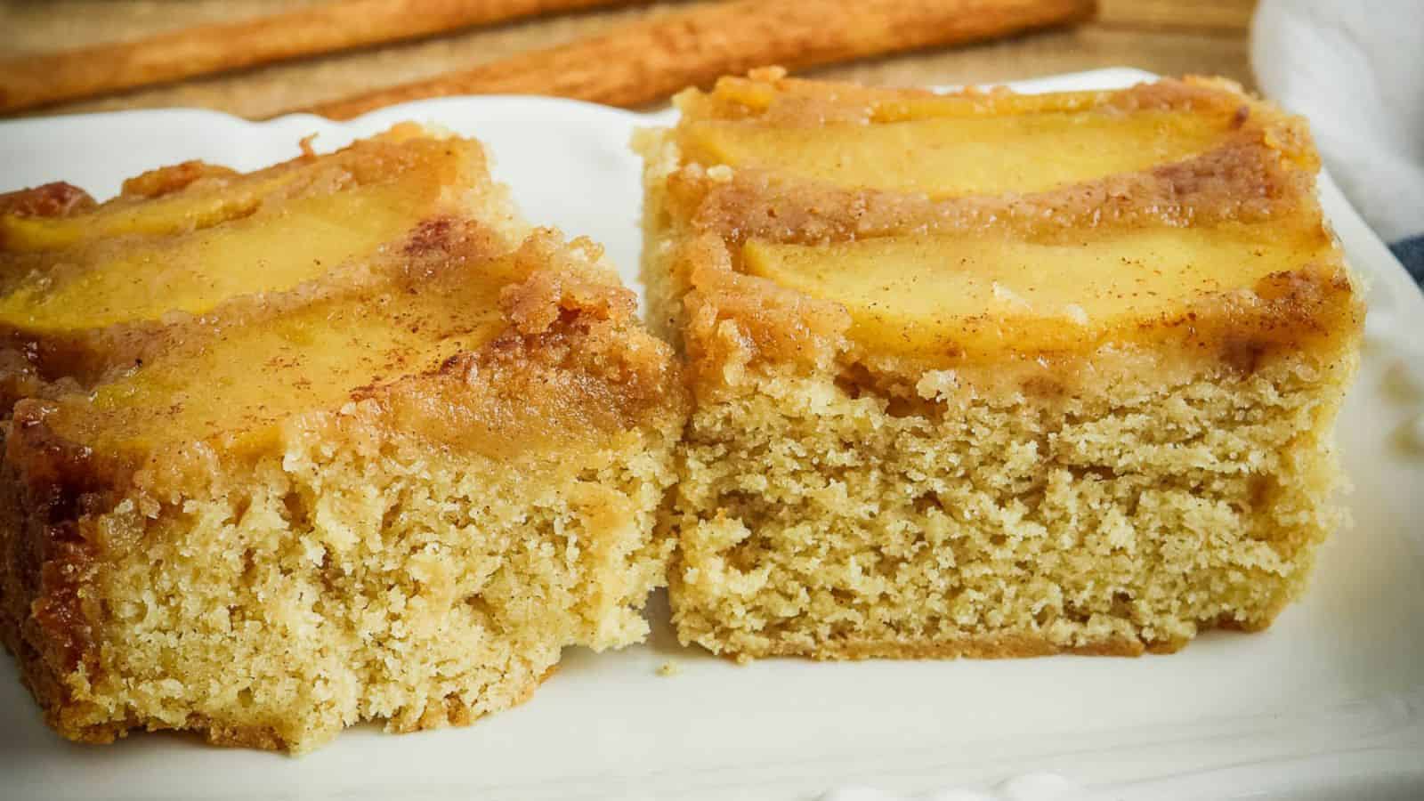 A slice of apple cake on a plate with cinnamon sticks.