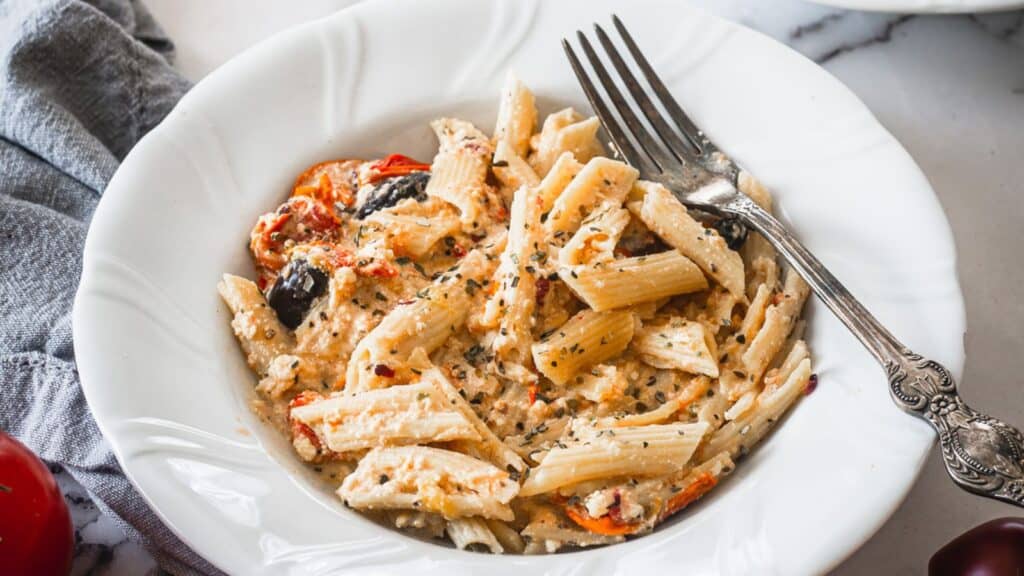A bowl of pasta with tomatoes and olives.