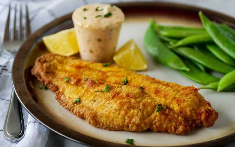 Fried fish fillet on a plate with lemon and green beans.