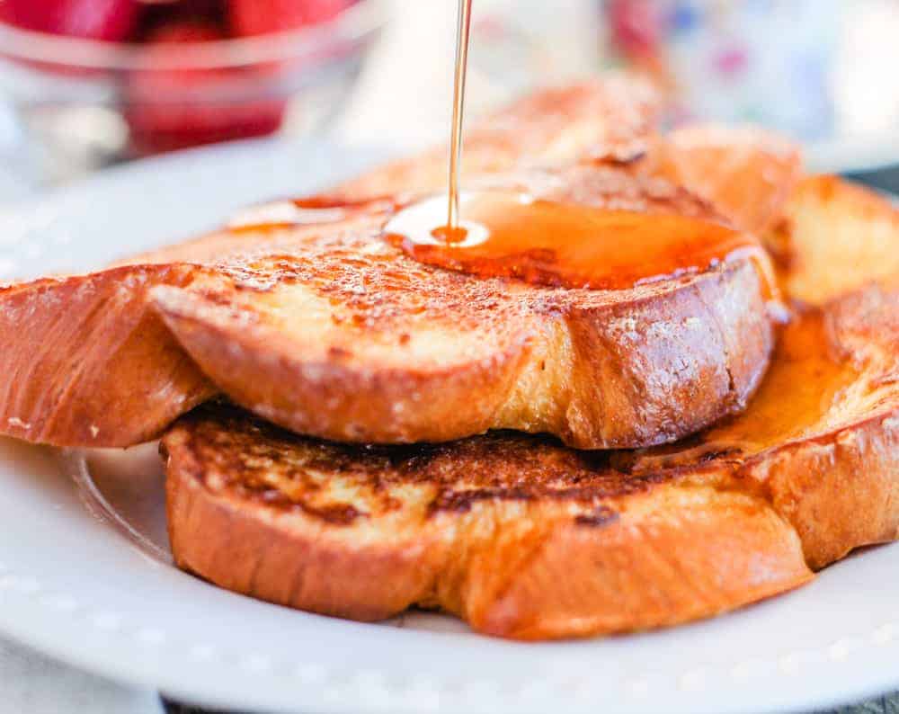 A plate of challah bread french toast being drizzled with maple syrup.