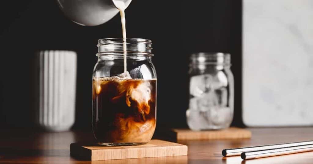 An iced coffee is being poured into a mason jar.