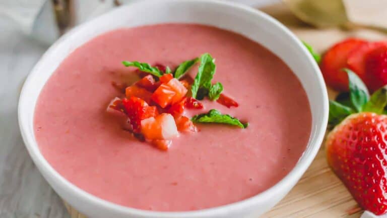 A bowl of strawberry soup with fresh strawberries.