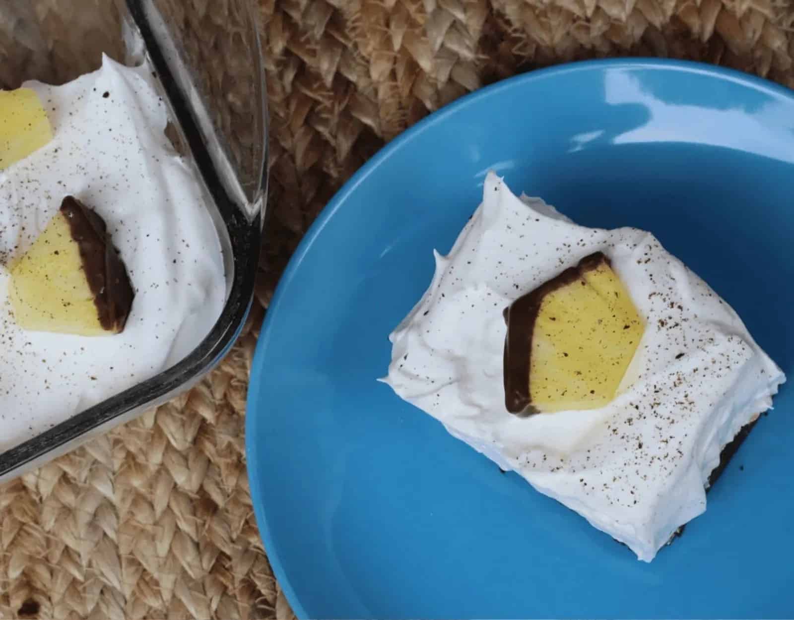 A piece of chocolate covered dessert on a plate next to a pan of dessert.