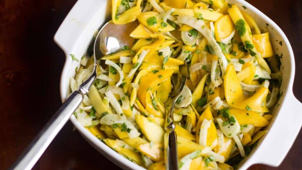 A white bowl of mango and onion salad with a spoon.