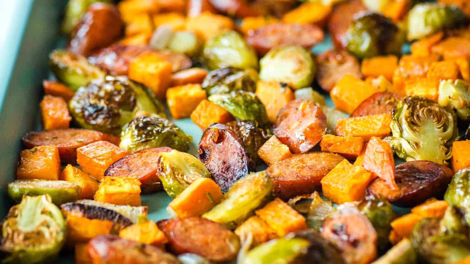 Roasted chicken apple sausage, sweet potatoes, Brussels sprouts and shallots on a sheet tray.