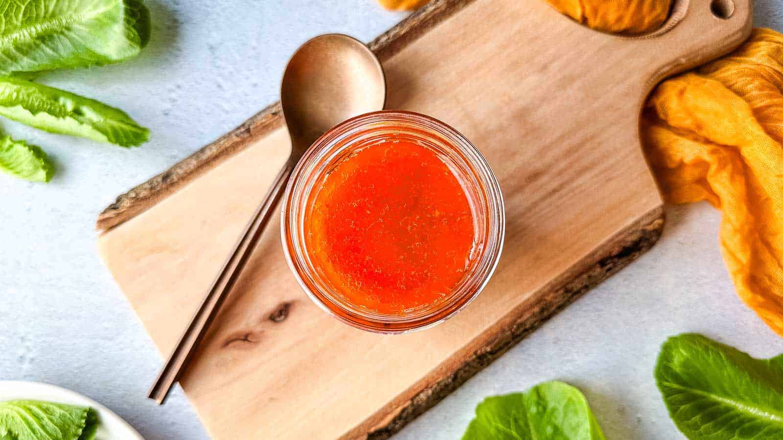 A jar of harissa vinaigrette on a wooden cutting board.