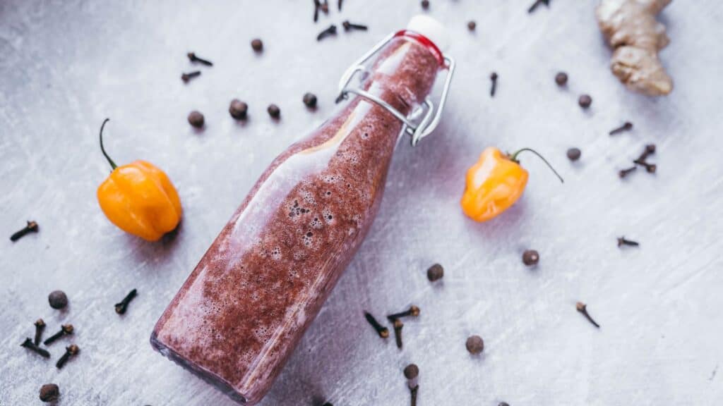 A bottle of chili sauce on a table with spices.