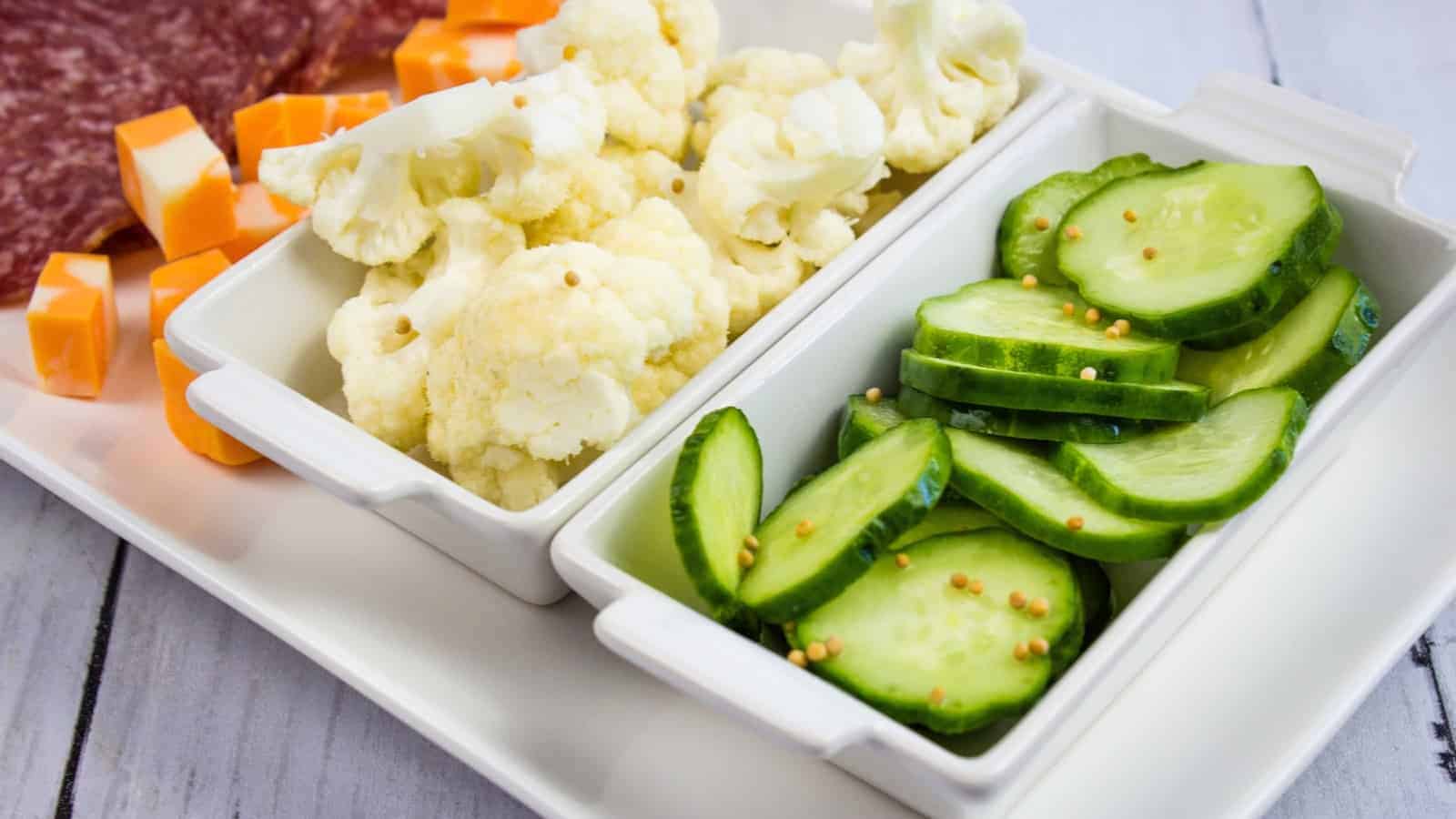 A plate with pickles, cauliflower, meat and cheese on it.