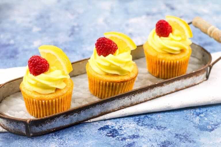 Three cupcakes with lemon icing and raspberries on a tray.