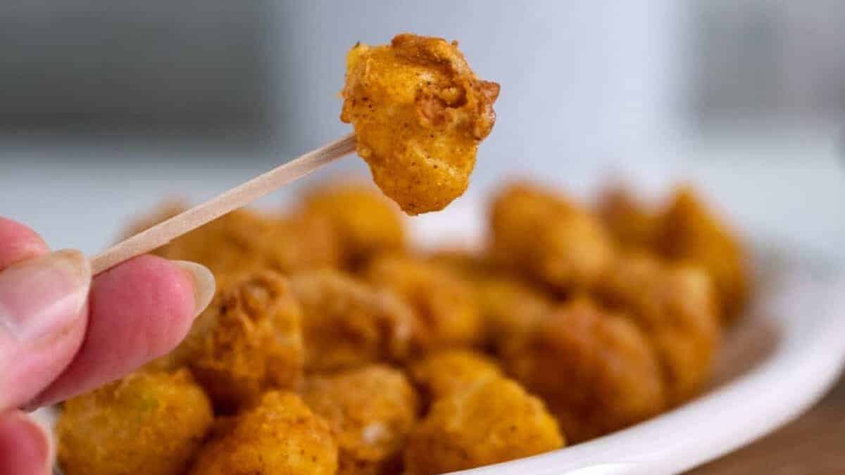 Air fried pearl onion on a toothpick with more fried onions on a plate in the background.