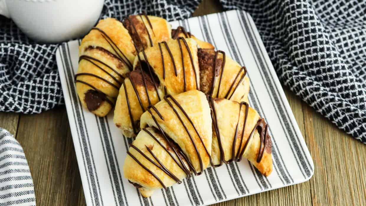 Three nutella crescent rolls on a plate drizzled with chocolate.