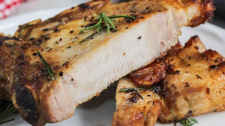 Pork chops on a plate with rosemary sprigs.