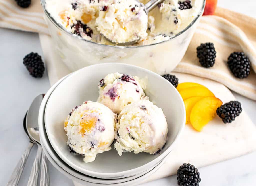 A bowl of ice cream with blackberries and peaches.