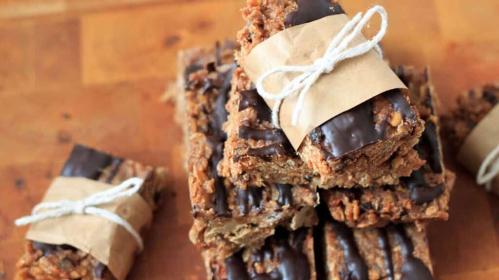 A stack of chocolate covered granola bars, a mouthwatering combination of indulgent chocolate and wholesome oats, arranged neatly on a cutting board.