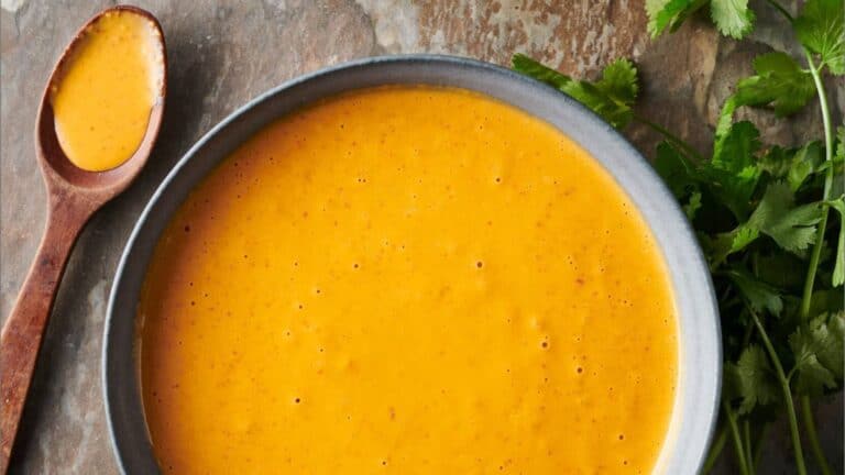 A bowl of peri peri sauce with a spoon on a wooden table.