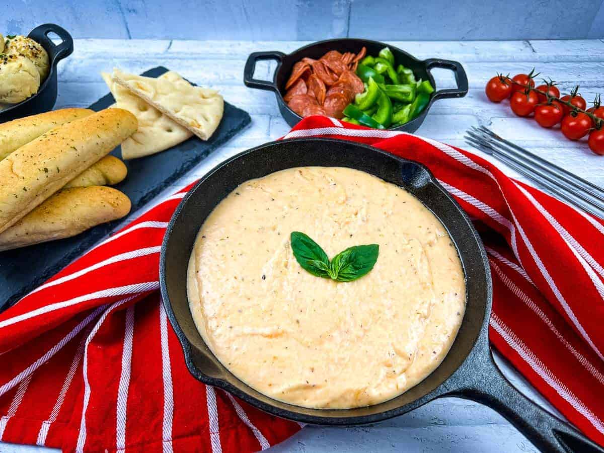 A skillet filled with pizza fondue and bread on a table.