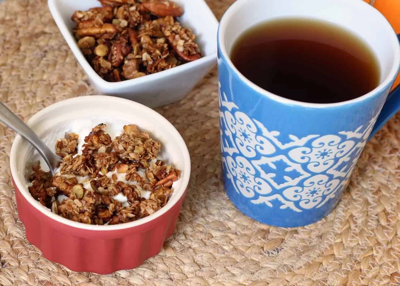 Bowl of yogurt topped with granola next to a cup of coffee.