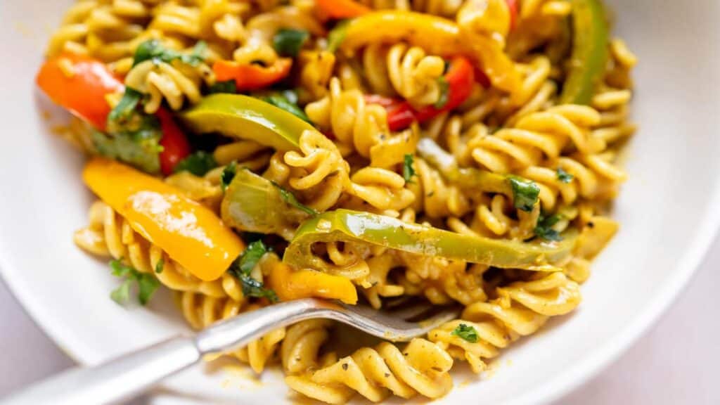 A plate of pasta with Caribbean vegetables and a fork.