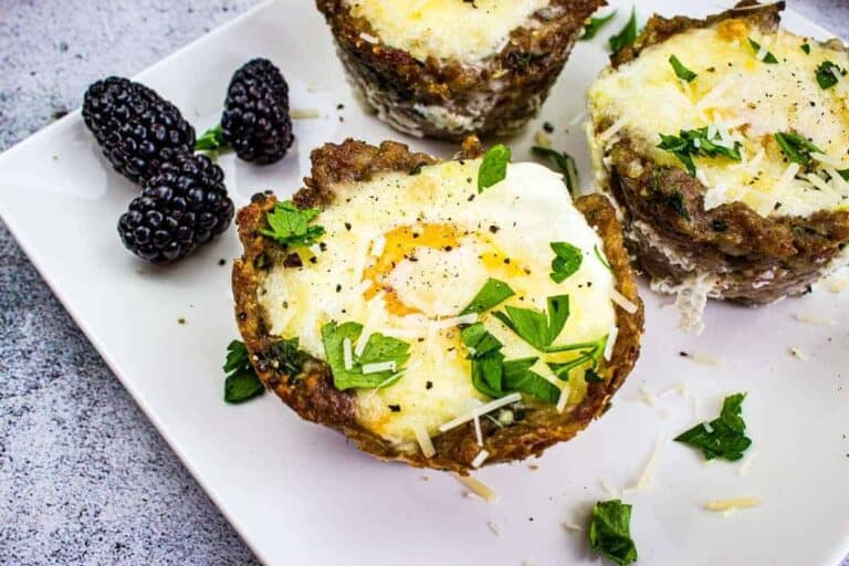 Three sausage n' egg cups with blackberries on a white plate.