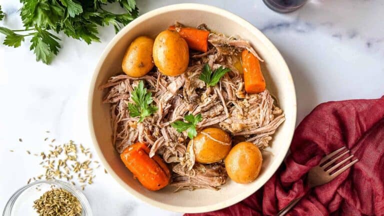 A white bowl with meat, potatoes and carrots.