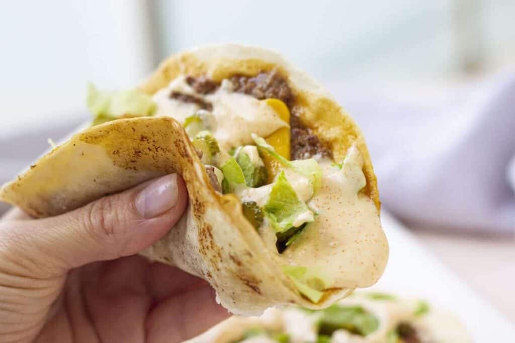 A person holding up a taco with lettuce and cheese.