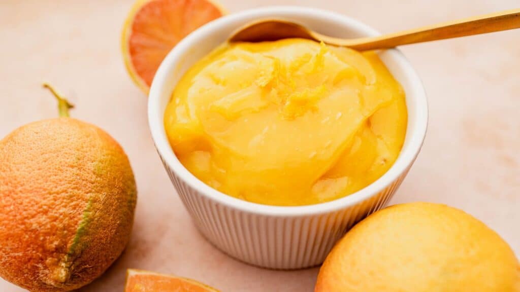 A bowl of orange juice with a spoon next to it.