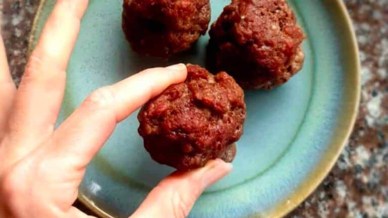 A person holding three meatballs on a plate.